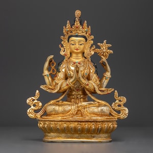 May include: A gold-coloured statue of a deity with four arms, wearing a crown and ornate jewellery. The statue is sitting in a lotus position on a decorative base.