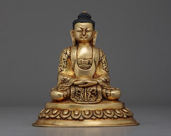 May include: A gold-coloured Buddha statue sitting in a meditative pose with a lotus base. The statue has intricate details and a black hair bun.