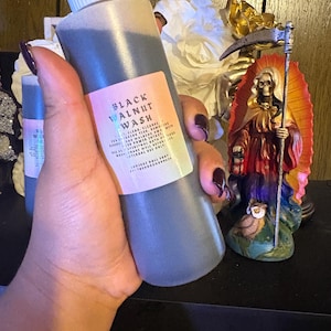 May include: A gray bottle of Black Walnut Wash with a white cap and a colorful label. The label includes the product name and other text. A statue of a robed figure with a scythe is in the background.