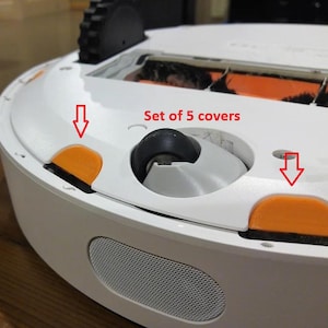 May include: A close-up of a white robotic vacuum cleaner with orange and black details. The image shows a set of five orange covers and the text "Set of 5 covers". The vacuum has a black wheel and a silver speaker.