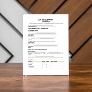 May include: A white document titled "APP DEVELOPMENT CONTRACT" stands upright on a wooden surface. The document contains lines for filling in information about the project, parties, and scope. The background features a mix of white and brown wooden panels.