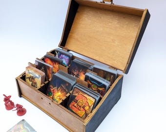 May include: Wooden card game storage box with a hinged lid, divided into compartments. The box is filled with various game cards featuring colorful fantasy art. Miniature red figurines are placed near the box.