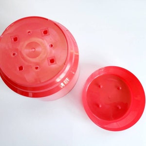 May include: Two red plastic plant pots, one larger than the other, with drainage holes in the bottom.