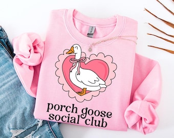 May include: Pink sweatshirt featuring a white goose inside a pink heart with the text "porch goose social club" in black.