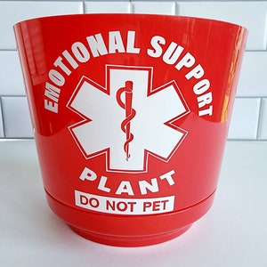 May include: Red plastic planter with a white star of life symbol and the text "Emotional Support Plant Do Not Pet".