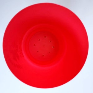 May include: A bright red plastic pot with drainage holes in the bottom. The pot is designed for planting small plants.