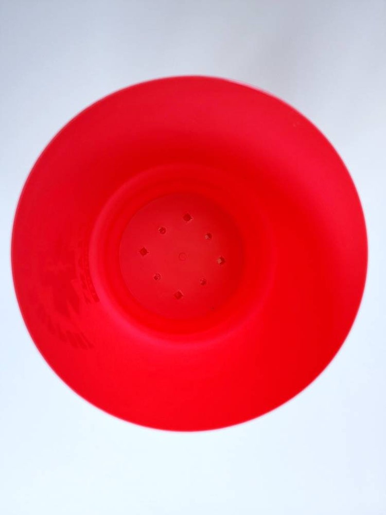 May include: A bright red plastic pot with drainage holes in the bottom. The pot is designed for planting small plants.