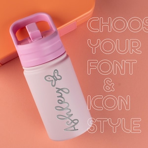 May include: A light pink water bottle with a matching pink lid and handle. The bottle features a gray butterfly icon and the name Ashley in a cursive script. The text CHOOSE YOUR FONT & ICON STYLE is displayed in white outline lettering.