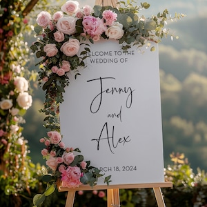May include: White wedding sign with pink and green floral decorations. The sign reads "Welcome to the wedding of Jenny and Alex, March 18, 2024".