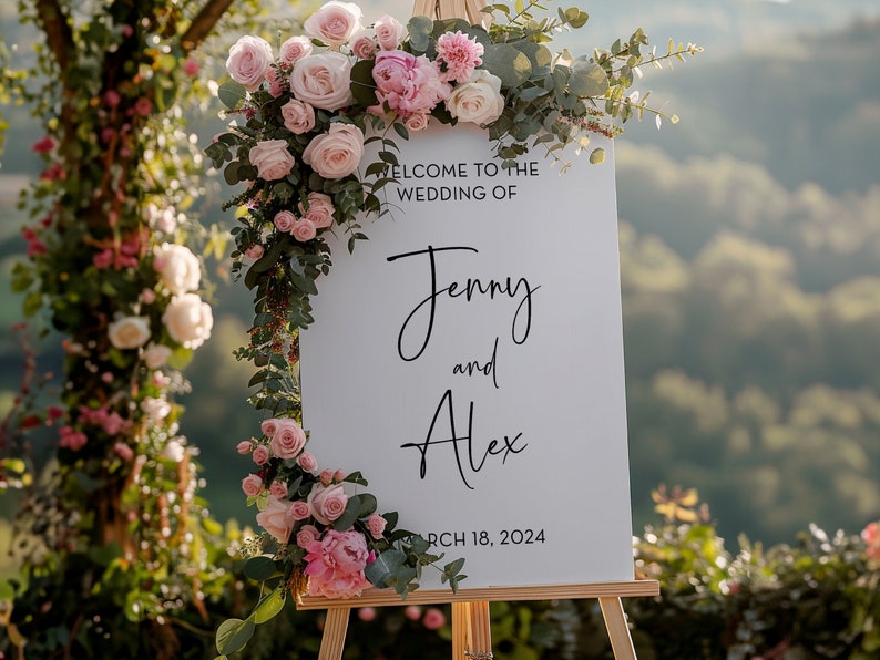 May include: White wedding sign with pink and green floral decorations. The sign reads "Welcome to the wedding of Jenny and Alex, March 18, 2024".