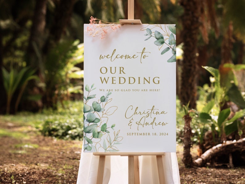 May include: A white wedding welcome sign with gold lettering and green watercolor foliage. The sign reads "Welcome to Our Wedding. We are so glad you are here! Christina & Andrew. September 18, 2024."