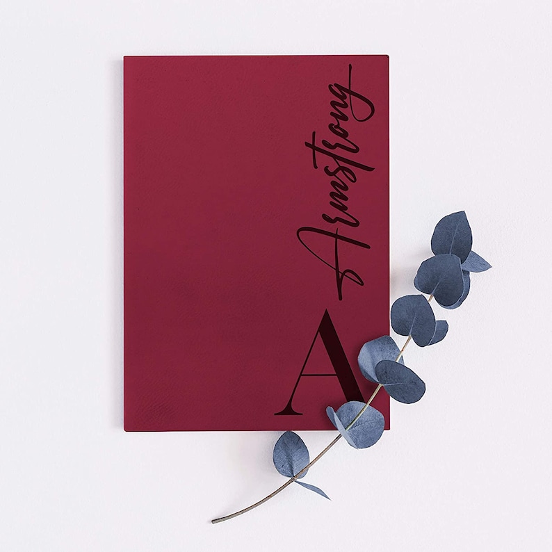 Pu&ograve; includere: Un quaderno color borgogna con il nome "Armstrong" scritto in corsivo nero sulla copertina. La lettera "A" &egrave; anche scritta in nero sulla copertina.