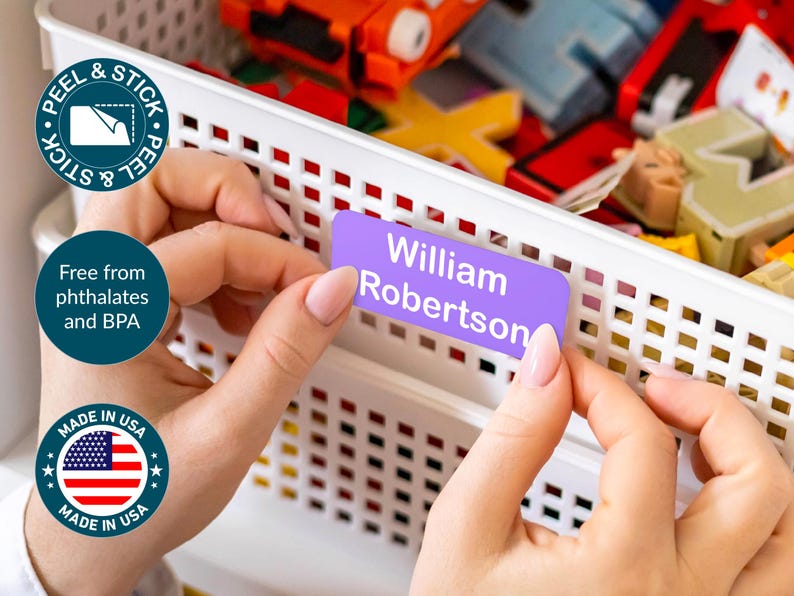 May include: A person is shown applying a purple label that reads "William Robertson" to a white storage bin. The label is peel and stick, and the product is made in the USA. The product is free from phthalates and BPA.