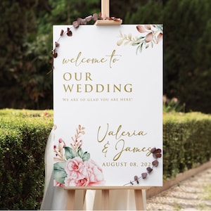May include: A white wedding welcome sign with gold lettering and watercolor floral illustrations. The sign reads "Welcome to Our Wedding, We are so glad you are here! Valeria & James, August 08, 2021".