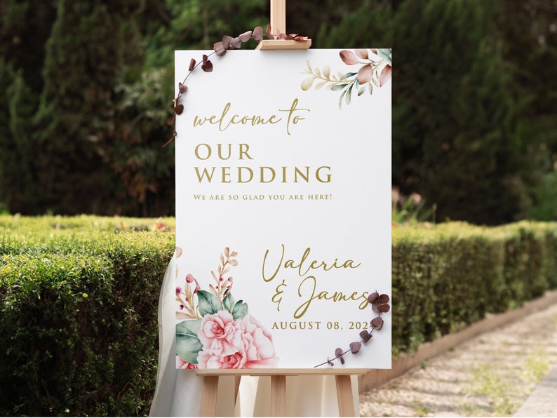 May include: A white wedding welcome sign with gold lettering and watercolor floral illustrations. The sign reads "Welcome to Our Wedding, We are so glad you are here! Valeria & James, August 08, 2021".