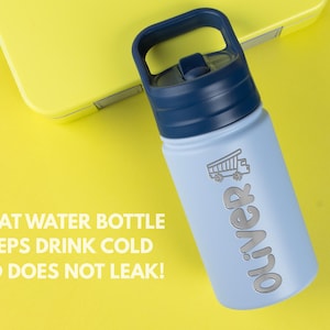 May include: A light blue water bottle with a dark blue lid and handle. The bottle features a graphic of a dump truck and the name Oliver in silver lettering. The text GREAT WATER BOTTLE KEEPS DRINK COLD AND DOES NOT LEAK! is visible.