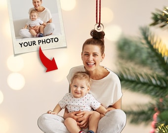 Puede incluir: Un adorno navideño con una foto de una madre y un niño. El adorno está hecho de metal y tiene una cuerda roja para colgar. La foto muestra a una mujer con cabello castaño sonriendo y sosteniendo a un niño pequeño. El niño lleva una camisa blanca con lunares negros. El adorno tiene el texto "YOUR PHOTO" impreso.