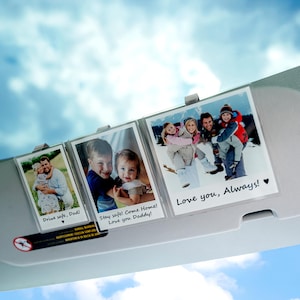 May include: Three photo display clips holding family photos. The photos have text that reads "Drive safe, Dad!", "Stay safe! Come Home! Love you Daddy!", and "Love you, Always!" The background is a blue sky.