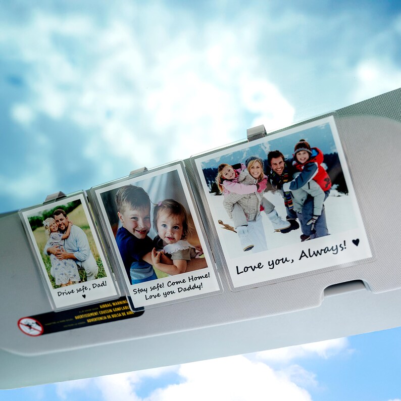 May include: Three photo display clips holding family photos. The photos have text that reads "Drive safe, Dad!", "Stay safe! Come Home! Love you Daddy!", and "Love you, Always!" The background is a blue sky.
