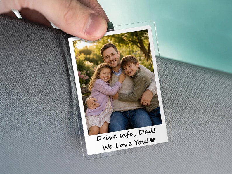 May include: A clear plastic photo holder with a family photo. The photo shows a man hugging two children. Text at the bottom reads "Drive safe, Dad! We Love You!" with a heart symbol. The holder is held by a hand.