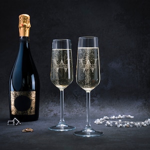 May include: Two champagne flutes with the word "Williams" etched on them, filled with sparkling wine. A bottle of champagne with a gold label is in the background.