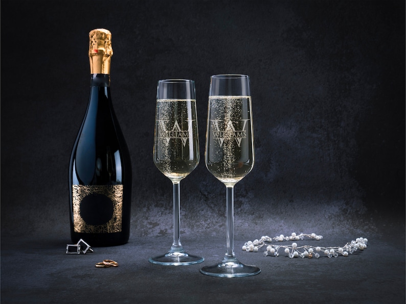 May include: Two champagne flutes with the word "Williams" etched on them, filled with sparkling wine. A bottle of champagne with a gold label is in the background.