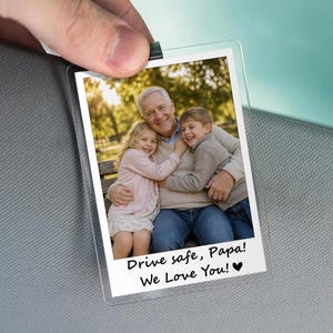 May include: A clear, rectangular photo holder with a family photo. The photo shows a grandfather hugging two grandchildren. Text at the bottom reads "Drive safe, Papa! We Love You!" with a heart symbol.