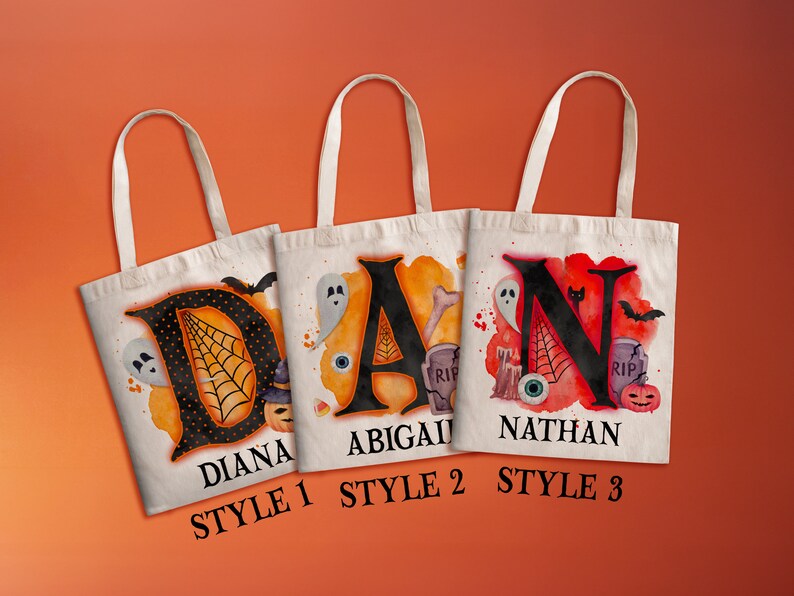 May include: Three Halloween-themed tote bags with different designs. The first bag features a black letter "D" with a spiderweb and a ghost, and the name "Diana" below. The second bag features a black letter "A" with a ghost, an eye, and a bone, and the name "Abigail" below. The third bag features a black letter "N" with a ghost, a bat, and a pumpkin, and the name "Nathan" below. Each bag has the words "Style 1", "Style 2", and "Style 3" below the name.