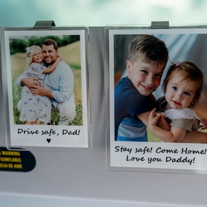 May include: Two clear photo holders clipped to a car visor. Each holder contains a photograph of children with the text "Drive safe, Dad!" and "Stay safe! Come Home! Love you Daddy!"