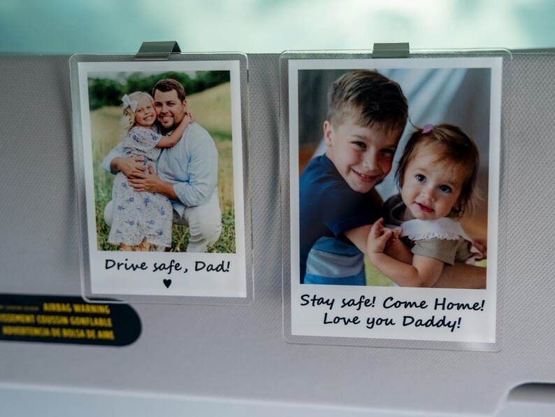 May include: Two clear photo holders clipped to a car visor. Each holder contains a photograph of children with the text "Drive safe, Dad!" and "Stay safe! Come Home! Love you Daddy!"