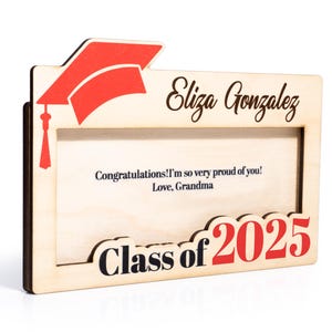 May include: Wooden picture frame with a graduation cap design. The frame has a space for a photo and a message. The message reads "Congratulations! I'm so very proud of you! Love, Grandma". The frame also has the text "Eliza Gonzalez" and "Class of 2025".