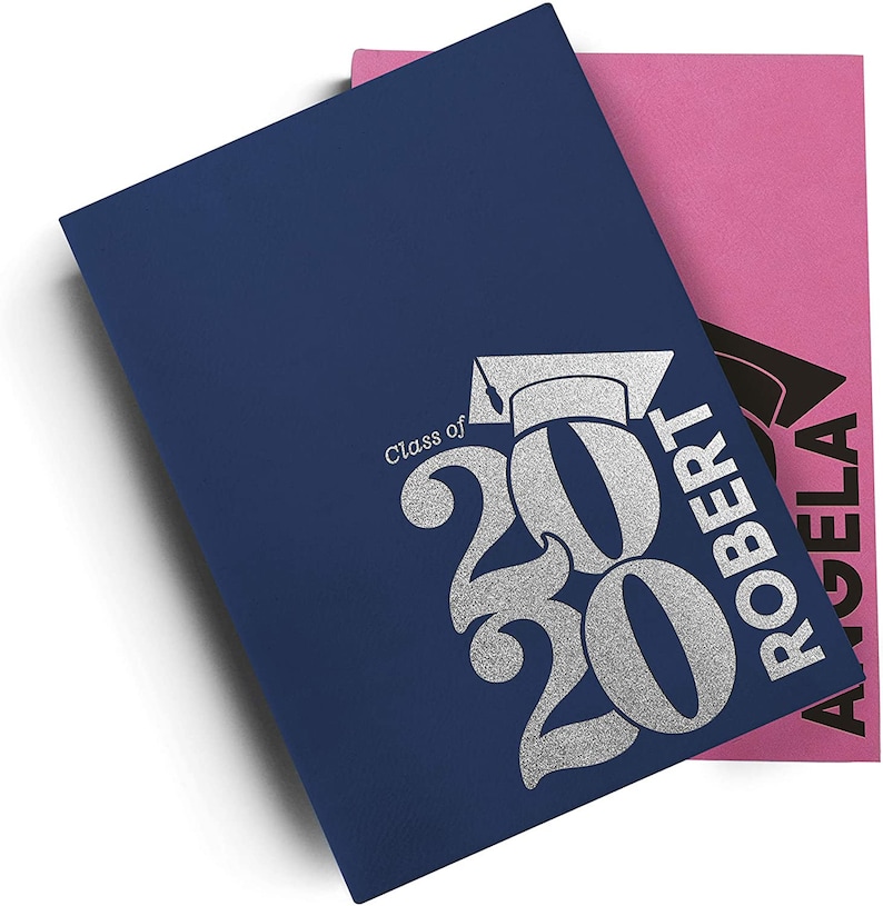 Pu&ograve; includere: Un biglietto di laurea blu con lettere argentate glitter che dicono "Classe del 2020" e un cappello di laurea. Il biglietto &egrave; piegato a met&agrave; e ha un biglietto rosa sopra con lettere nere che dicono "Angela Robert".