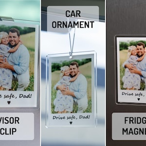 May include: A personalized photo gift featuring a picture of a father and child. The image is available as a visor clip, car ornament, and fridge magnet. Each item has the text "Drive safe, Dad!" and a heart symbol.