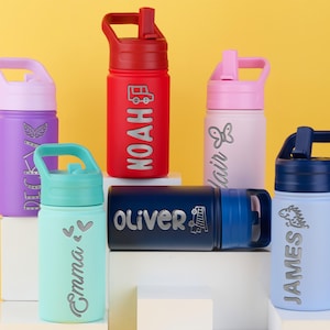 May include: Six colorful water bottles with lids and handles, each featuring a unique name and graphic. The bottles are purple, red, light pink, teal, dark blue, and light blue, with silver-toned engraved names including Noah, Oliver, and James.