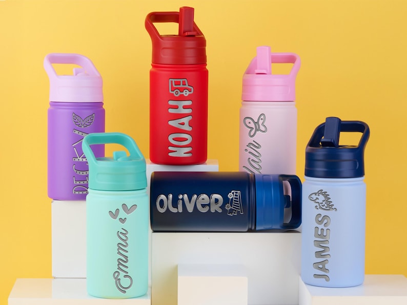 May include: Six colorful water bottles with lids and handles, each featuring a unique name and graphic. The bottles are purple, red, light pink, teal, dark blue, and light blue, with silver-toned engraved names including Noah, Oliver, and James.