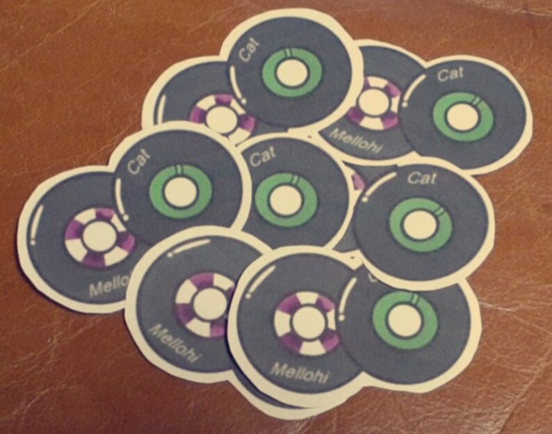 May include: A stack of round, black and white stickers with green and purple accents. The stickers have the words "Cat" and "Mellohi" printed on them.