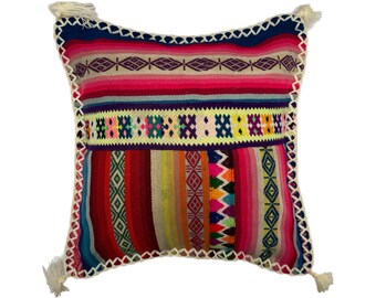 May include: A colorful throw pillow with a geometric pattern in shades of pink, red, yellow, green, and blue. The pillow has a white fringe border and tassels on the corners.
