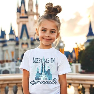 May include: A young person wearing a white t-shirt with the text "Meet Me In Arendelle" in a stylized font. The shirt features a castle design in shades of blue and teal. The background shows a large castle.