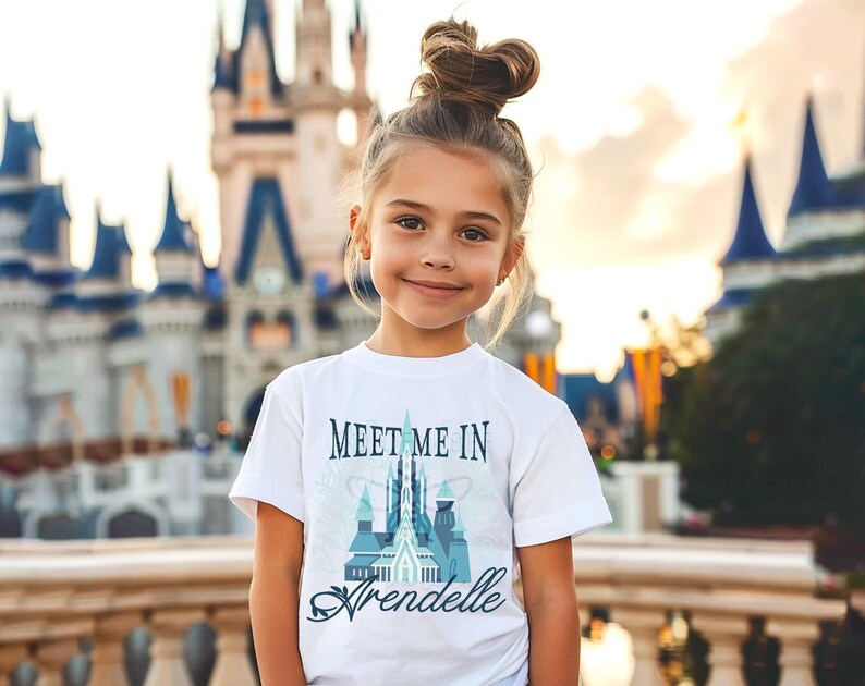 May include: A young person wearing a white t-shirt with the text "Meet Me In Arendelle" in a stylized font. The shirt features a castle design in shades of blue and teal. The background shows a large castle.