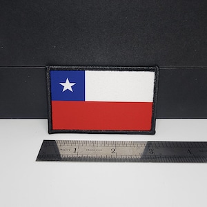 May include: Embroidered patch featuring the flag of Chile. The rectangular patch has a blue square with a white star in the upper left corner, a white stripe, and a red stripe. The patch is approximately 3 inches wide.