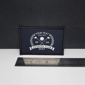 May include: A rectangular navy blue patch with a white golf-themed design. The design includes crossed golf clubs, a golf ball, laurel branches, and the text "YOUR TEXT", "COUNTRY CLUB GOLF", and the numbers "20" and "24". The patch is approximately 3 inches wide.