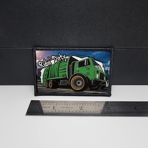 May include: Embroidered patch featuring a green garbage truck with gold rims, set against a cityscape backdrop. The patch has the words "Ridin' Dirty" in white script. The patch is approximately 3 inches wide.