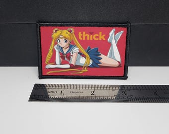 May include: A rectangular patch with a black border features an anime-style illustration of a character in a sailor uniform, lying down on a red background. The word "thick" is written in yellow. A ruler is placed below the patch.