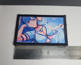 May include: A rectangular patch featuring an anime-style illustration of a woman with blue hair and clothing. The patch has a black border and the word "thick" is visible. The patch is approximately 3 inches wide.