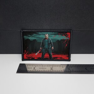 May include: A rectangular patch featuring a horror movie character with a hockey mask, holding a weapon. The background shows a cityscape with red splatters. The patch is approximately 3 inches wide.