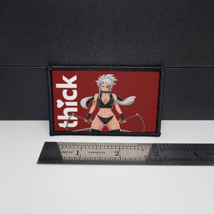 May include: A rectangular patch with a black border and a red background. The patch features a stylized anime-style illustration of a person in black lingerie holding chains. The word "thick" is printed in white on the left side. A stainless steel ruler is below the patch.