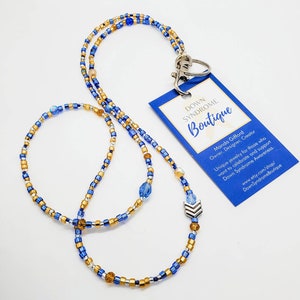 May include: A blue and gold beaded lanyard with a silver charm and a tag that reads "Down Syndrome Boutique". Manda Gifford, Owner, Designer, Creator. Unique jewellery for those who want to celebrate and support Down Syndrome Awareness. www.etsy.com/shop/DownSyndromeBoutique