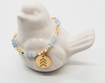 May include: A gold bracelet with light blue beads and a gold charm with a triangle design.