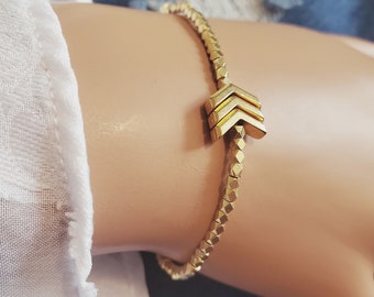 May include: A gold bracelet with a geometric arrow charm. The bracelet is made of small, faceted beads.
