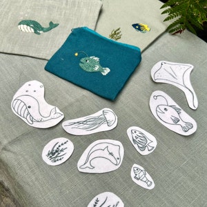 May include: A set of 10 iron-on patches featuring various sea creatures, including whales, fish, jellyfish, and seaweed. The patches are white with black embroidery and are perfect for adding a nautical touch to clothing, bags, or other fabric items.